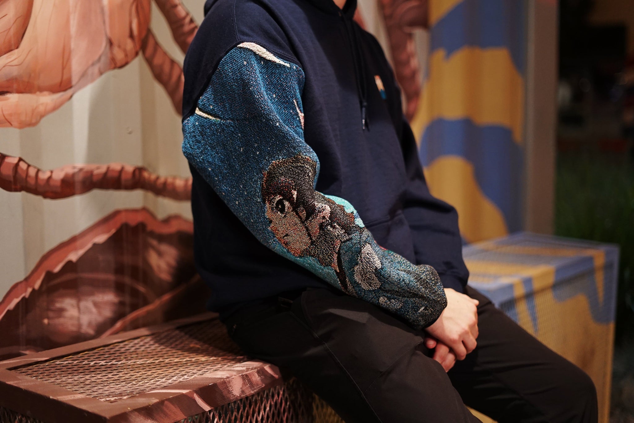Person modeling the Tanji Tapestry Sleeve Hoodie sitting down 