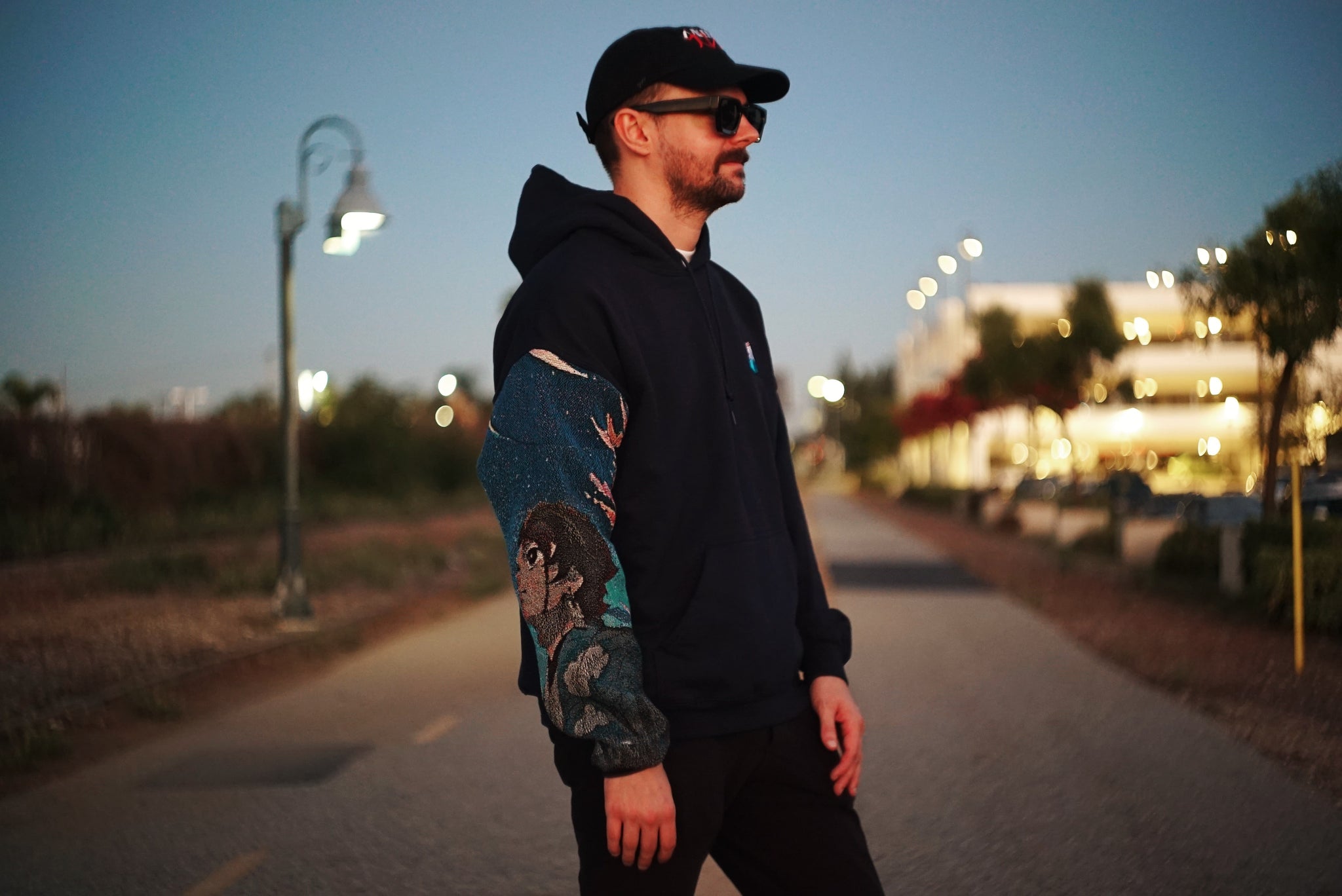 Male model wearing Tanji Tapestry Sleeve Hoodie on a walkway at sunset