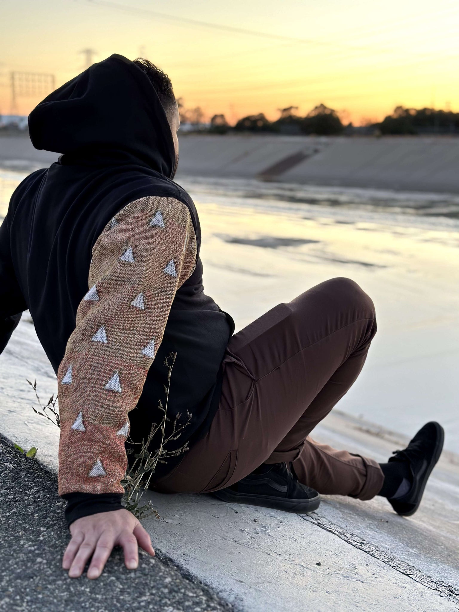 Male model wearing Zen Tapestry Sleeve Hoodie while sitting in a river bed at sunset